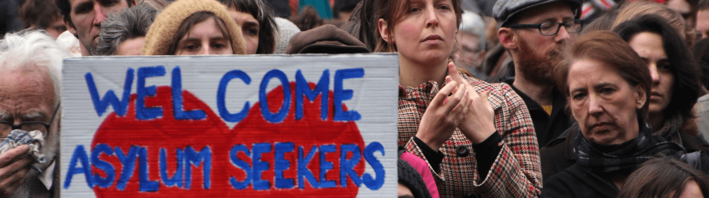 People at protest holding sign that says "Welcome Asylum Seekers".