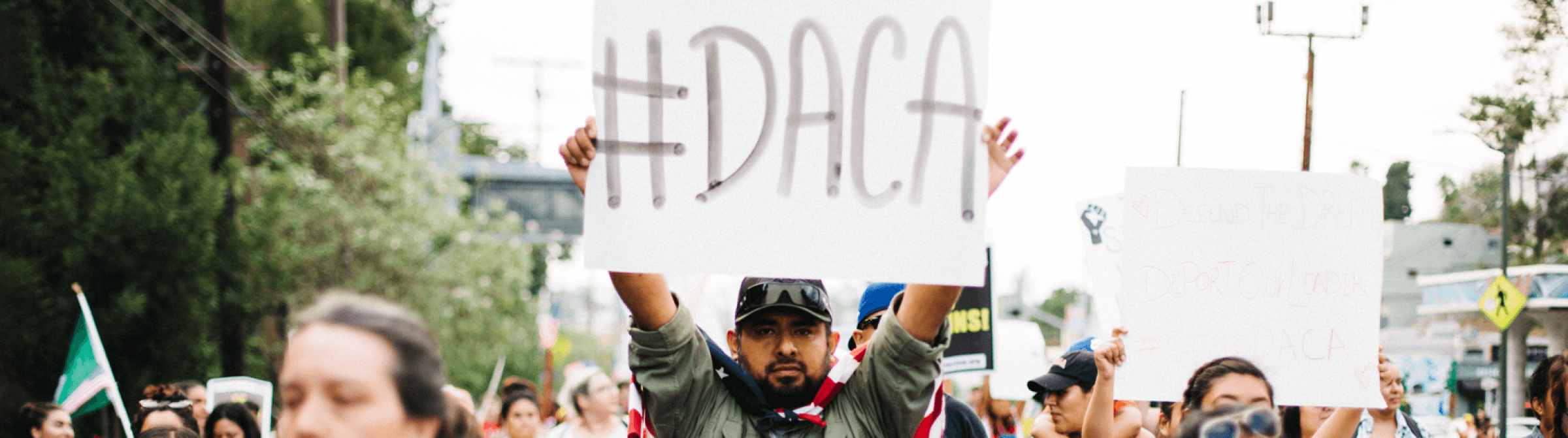 Image of protestor holding a sign that says "#DACA" on it.