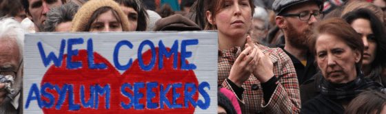 People at protest holding sign that says "Welcome Asylum Seekers".