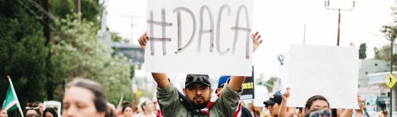 Image of protestor holding a sign that says "#DACA" on it.