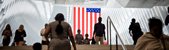 People walking up and down stairs in front of an American flag.