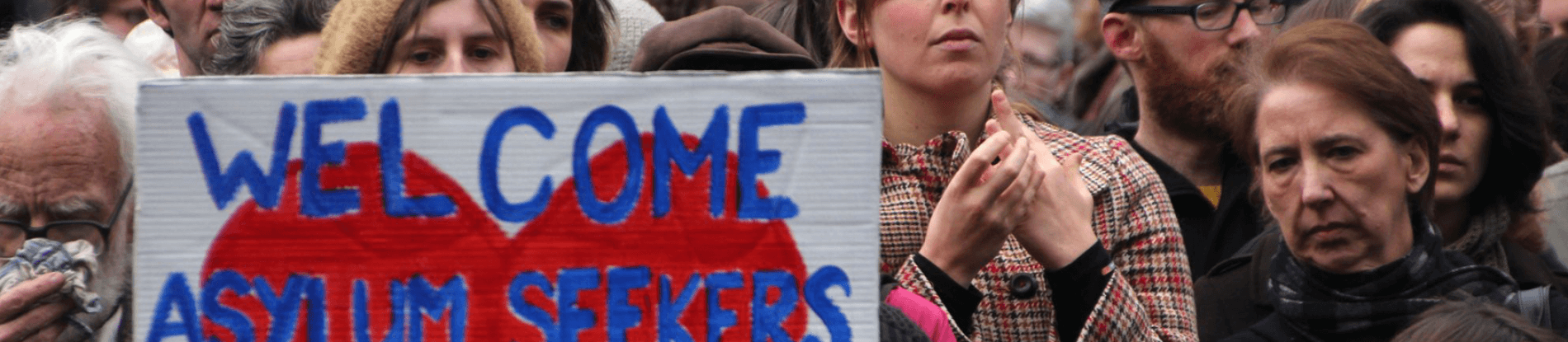 People at protest holding sign that says "Welcome Asylum Seekers".
