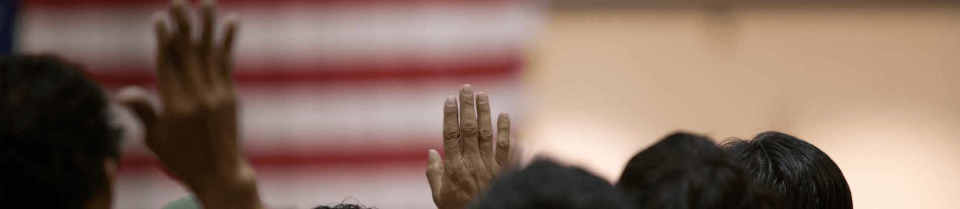 Picture of people raising their hands in front of an American flag.