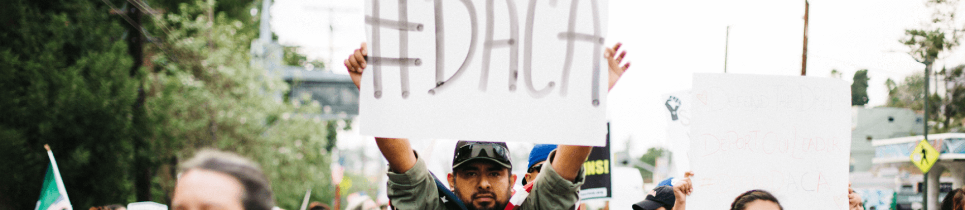 Image of protestor holding a sign that says "#DACA" on it.